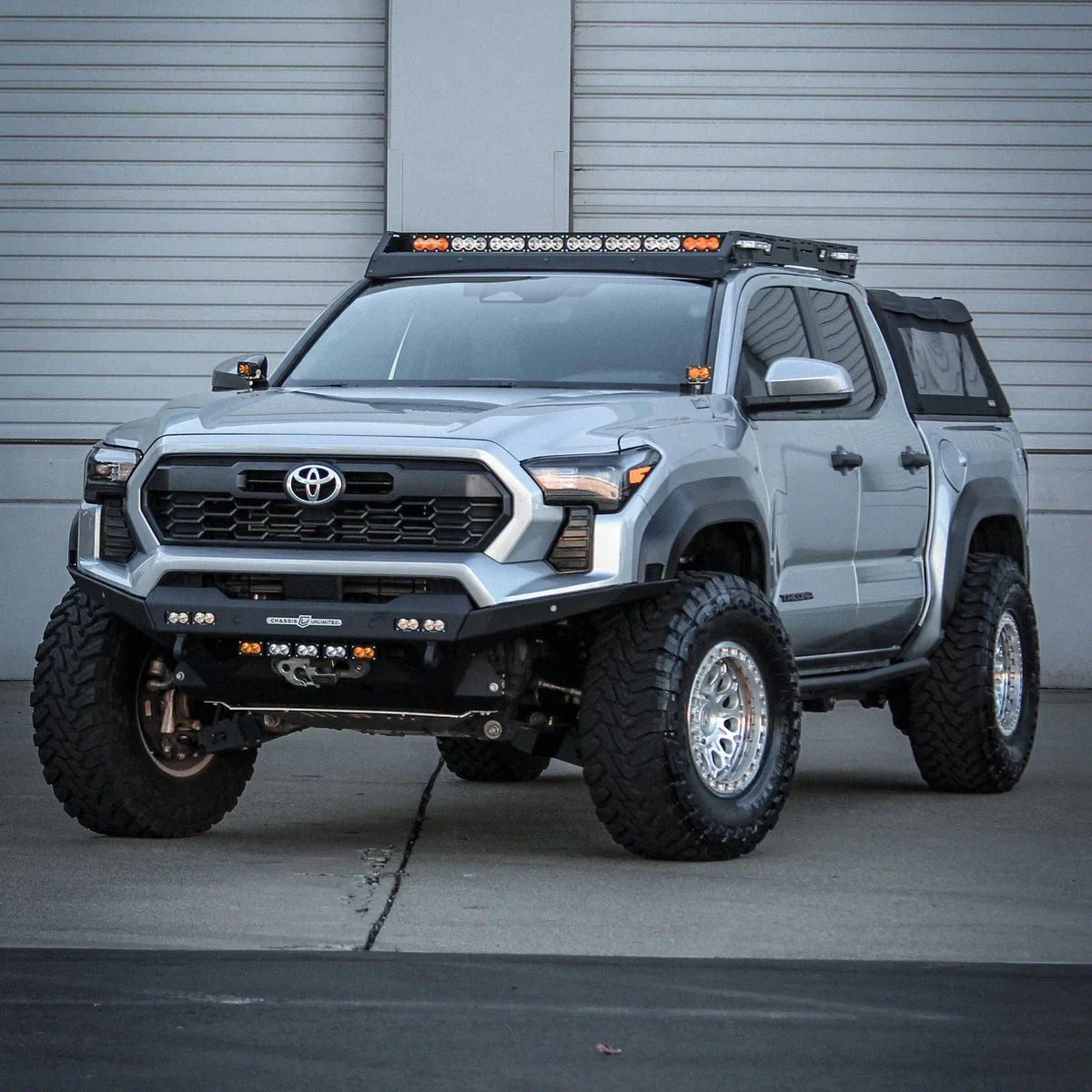 Fully built 3rd Gen Toyota Tacoma featuring a suspension lift kit, Prinsu roof rack, and a steel front bumper with high-clearance wings. Equipped with a dual-function LED light bar, matte black off-road wheels, and aggressive all-terrain tires.