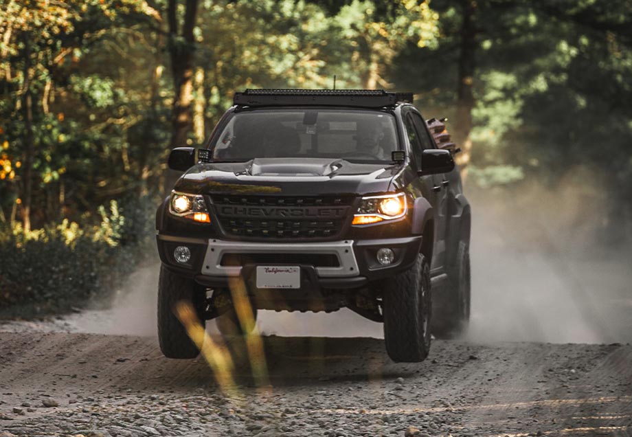 chevy truck with morimoto headlights on off road trail taking a jump and in mid air.