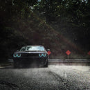 Front view of a black Dodge Challenger, with cyan LED headlight halo rings installed.