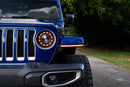Close-up of a blue Jeep Wrangler JL with the Morimoto Fender chop kit with XRGB lighting on a road with trees in the background.