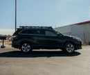 Black SUV with a roof rack on a paved surface with a clear sky.