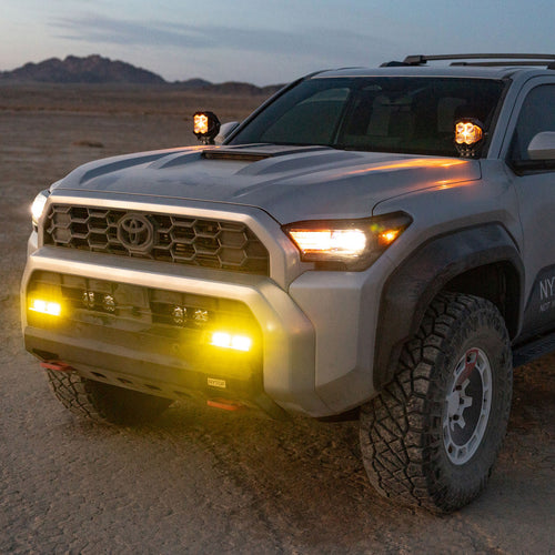 White 2025 Toyota 4Runner SUV with illuminated headlights in a desert landscape