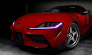 Close-up on the front end of a red Toyota Supra, with pink headlight DRLs.