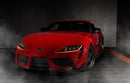 Three quarters view of a red Toyota Supra with amber headlight DRLs.