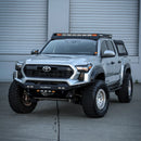 Gray 2024 Toyota Tacoma with off-road modifications in front of a gray building.