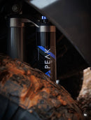 Close-up of the Peak Suspension 2.5″ DSC Coilover Trail Kit with a muddy tire in the foreground on a 2021 Ford F-150.