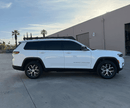 White Jeep Grand Cherokee L mounted with a prinsu roof rack parked in a lot with palm trees and a building in the background