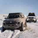 Two toyota tacoma offroad vehicles driving through the snow