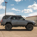 Gray Toyota 4Runner with large tires and a roof rack on a concrete surface under a blue sky.