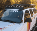 White Toyota Tacoma with roof rack and 'Nitto' branding in a forest setting