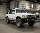 White 4Runner SUV with large off-road tires and a Prinsu Roof Rack in a warehouse setting