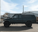 Toyota Tacoma pickup truck with a prinsu roof rack parked on a concrete surface with a building and sky in the background